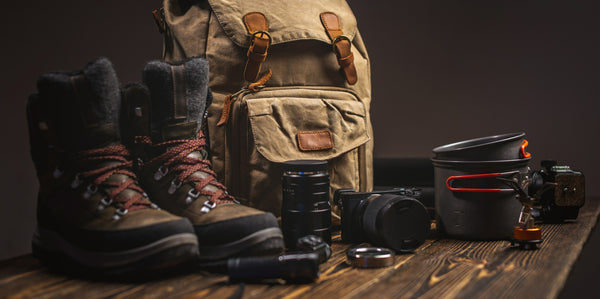 Pair of hiking boots, backpack, camera, and other gear on a wooden surface with a dark background