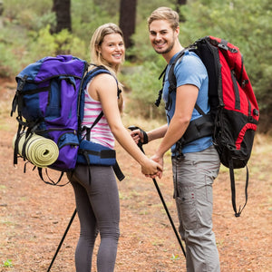 Two hikers with backpacks and walking sticks on a trail in a forest.